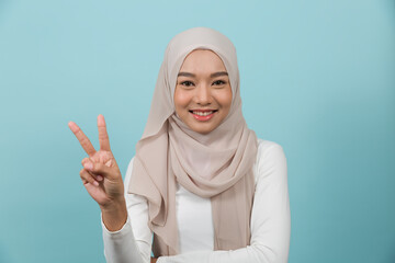 Asian young Muslim woman wearing traditional islamic hijab headscarf showing and pointing up with her fingers number two. Muslim woman showing fingers number two against blue colour background