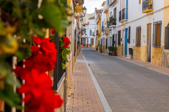 Narrow streets of a Mediterranean village, with balconies and windows adorned with plants and flowers, on a sunny afternoon. In La Nucia, Alicante (Spain).