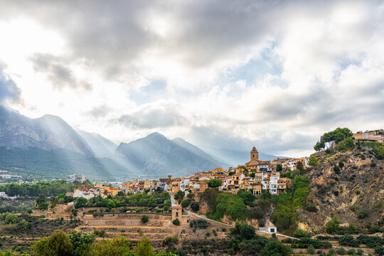 Nice landscape with the picturesque town of Polop in Alicante (Spain), with the sun's rays passing through the mountains and the clouds.