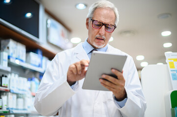 Senior pharmacist working on tablet in his store