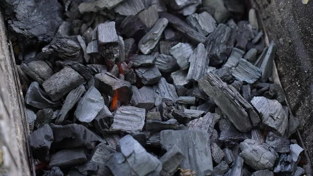 Closeup top view 4k video footage of bbq pit full of black organic charcoal briquettes flaming and burning ready to cook food outdoors during picnic getaway