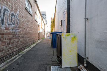 Discarded fridge seen in a narrow alleyway in a city centre. Graffiti and waste bins can also be...