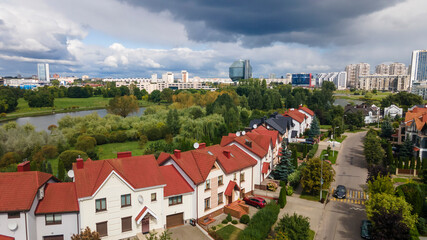 Panoramic view of a new neighborhood cottage village in the foreground and the modern building of national library of Belarus in the background. Dramatic sky background.