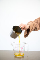 Woman pours used cooking oil from metal container into measuring container
