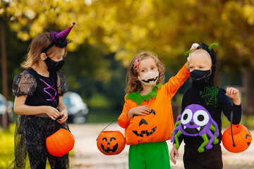 Three kid with a basket for sweets making grimaces wearing face mask on Halloween holiday - obrazy, fototapety, plakaty