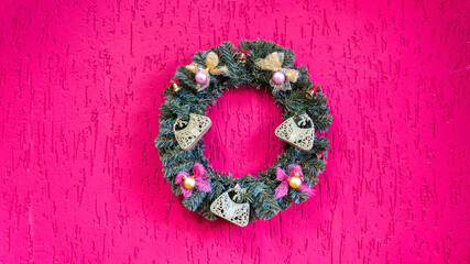 Beautiful Christmas and New Year wreath on pink concrete wall. Stylish rustic christmas wreath with pine cones, fir branches, snow, hanging on red wall. Space for text.