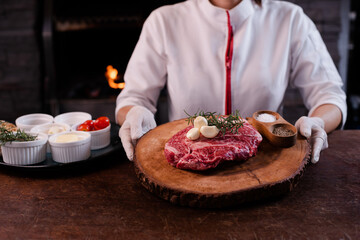 Wagyu chuck steak on a wooden cutting board Garnish with rosemary and garlic. chef standing in the back