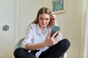 Emotional young beautiful woman looking at smartphone screen