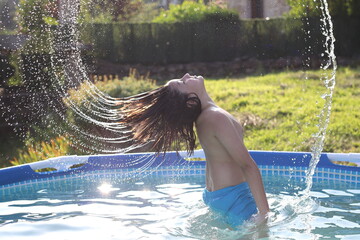 niño con el pelo largo salpicando en la piscina