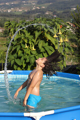 niño con el pelo largo salpicando en la piscina - 455136794