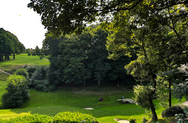 Looking across a golf course, with a gardener, old trees, and broken sunlight in, Bradford, Yorkshire, UK