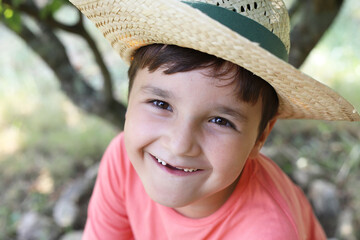 niño con gorro de paja sonriendo sin algunos dientes de leche en la naturaleza - 455137799