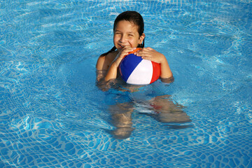 niño con pelo largo jugando a la pelota en la piscina