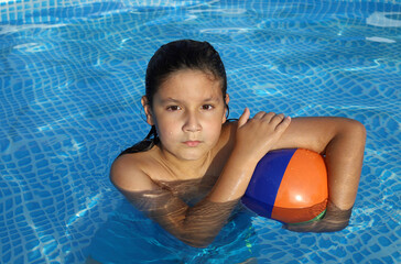 niño con pelo largo jugando a la pelota en la piscina - 455137940