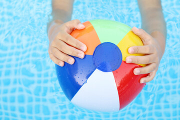 manos de niño sujetando una pelota hinchable de colores en la piscina