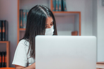 Niña adolescente joven con mascarilla estudiando para el examen en la clase del campus universitario con libros y ordenador portatil laptop