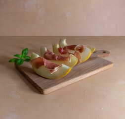 Antipasti fresh melon with prosciutto and basil on the wooden board