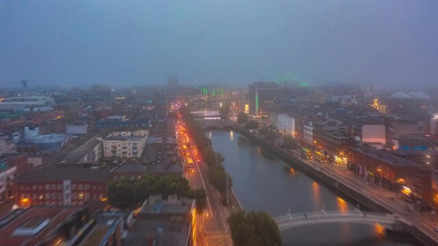 Forwards fly above River Liffey. Aerial hyperlapse footage of evening traffic on waterfront illuminated by street lights. Low clouds above city. Dublin, Ireland