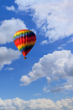 A multicolored hot air balloon raises a basket with tourists in the blue sky. Vertical image.