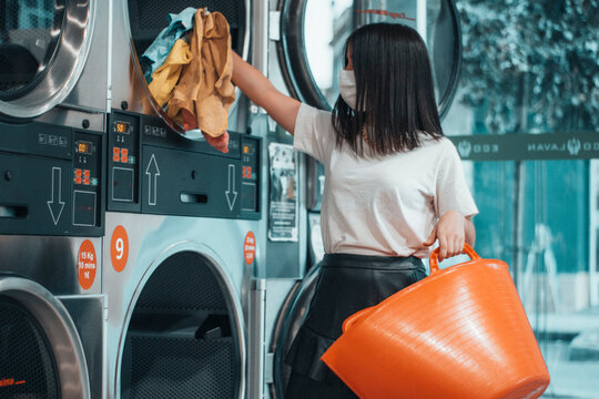 Joven adolescente de pelo casta&ntilde;o a&ntilde;adiendo prendas de ropa en la lavanderia industrial junto con otros quimicos como detergente para lavar la indumentaria 