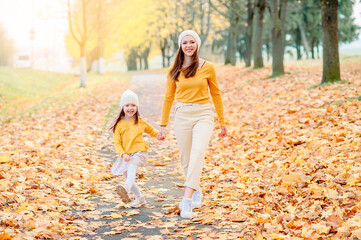Fototapeta premium mom in a knitted hat with her daughter walking looking into the lens in the autumn park with a wide smile
