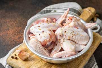 Raw chicken wings in a metal bowl on a wooden board on a dark culinary background. The process of cooking poultry	