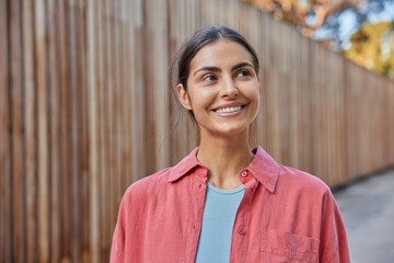 Outdoor shot of happy young woman in casual apparel walks around urban setting returns glad after...