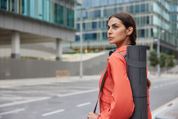 Sporty woman walks on city road alone prepares for training outdoor chooses place for exercise dressed in sportswear does yoga in urban background enjoys healthy lifestyle. Wellness concept.