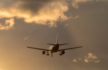 Naklejka na ściany i meble Silhouette of the airplane in the sunset colored clody sky