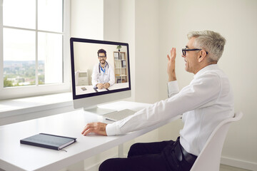 Senior Caucasian businessman sitting in the office talking to his doctor by video link. Male doctor provides online consultation to his patient. Concept of online medical consultation.