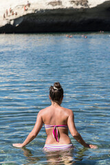 Woman in bathing suit shot from behind enters the sea in Sardinia. Beach holidays concept.