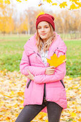 Happy young woman playing with falling yellow leaves in beautiful autumn park on nature walks outdoors. Teenage girl holding autumn orange maple leaf.