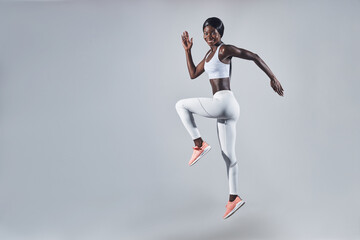 Fototapeta na wymiar Full length of confident young African woman in sports clothing jumping against gray background