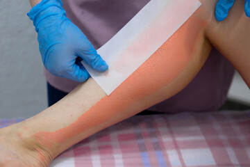 Epilation on the legs.Removal of unwanted hair on the legs.The master removes the wax with the help of special bandage strips for depilation.A girl in disposable gloves pasted a strip for depilation