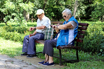 Elderly couple sitting on a bench and looking at watch. Leisure in park, life in retirement