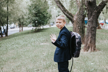 Fototapeta premium cute blond boy in a school uniform and with backpack on his shoulders goes to school at the beginning of the new school year, back to school concept and no desire to study