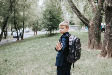cute blond boy in a school uniform and with backpack on his shoulders goes to school at the...