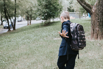 cute blond boy in a school uniform and with backpack on his shoulders goes to school at the...