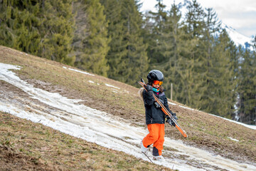 Child holding ski and walking on grass. Problem of global warming and winter skiing.