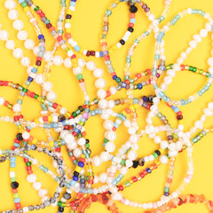 Closeup of necklaces made from multicolored beads and pearls on a yellow background.