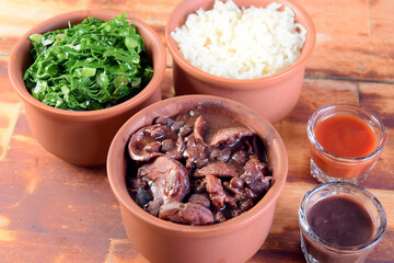 typical Brazilian food feijoada made with beans, pork, bacon, sausage with cabbage, rice, salad, spices and pepper.