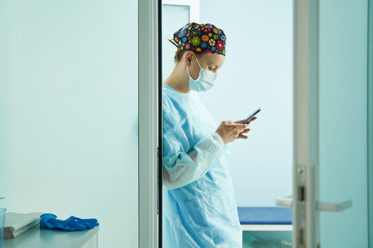 Surgeon in uniform chatting on smartphone in hospital