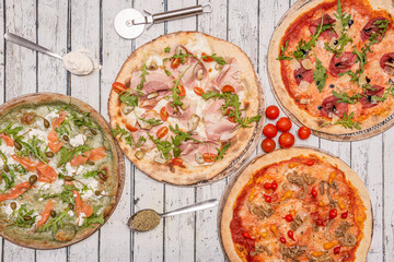 top view image of Italian pizzas of different flavors with flour and oregano in spoons. Arugula and cheese with Norwegian salmon, ham and loin and cherry tomatoes, melted cheese and pickled