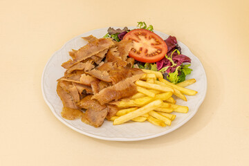 Kebab plate with spiced roast lamb slices, fried potatoes and oak salad and tomato slices in a restaurant doner kebab on white plate
