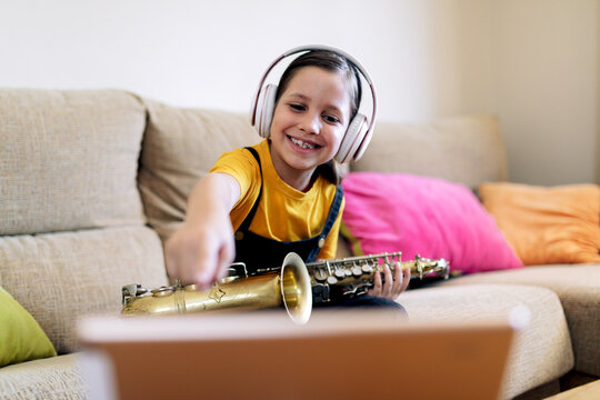 Concentrated girl in headset with saxophone on sofa against smartphone