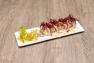 Sushi uramaki roll with avocado and surimi, nori seaweed, sauces and tengusa red seaweed on top
