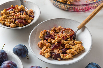 Plum crumble dessert in plates with spoons on white background for tasty breakfast