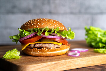 hamburger with cutlet, tomato, cheese and lettuce leaves on a wooden board