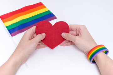 A woman wearing lgbtq rainbow bracelet holding a heart