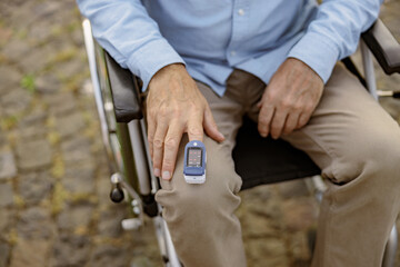 Close up shot of hand of handicapped man in wheelchair using fingertip pulse oximeter for measuring...